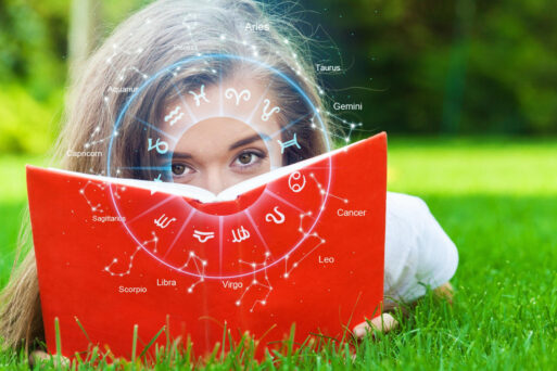 Девушка лежит на зеленой траве с книгой, украшенной знаками зодиака, погружаясь в чтение гороскопа на май под открытым небом.